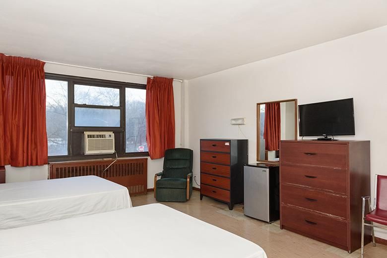 A hotel room with two beds, an air conditioner, and various pieces of furniture including a dresser and television.