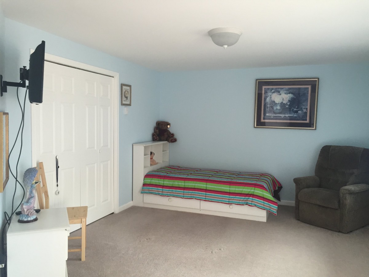 A simple bedroom with a single bed, blue walls, and a cozy chair.