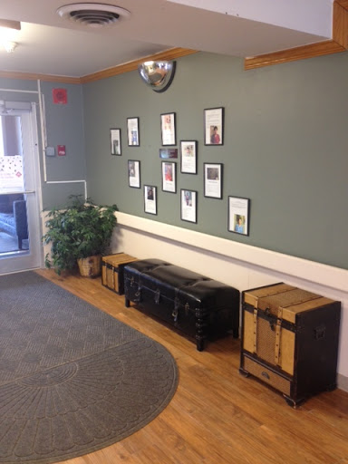 A cozy waiting area featuring a green wall adorned with framed photographs, complemented by wooden seating and a decorative plant.