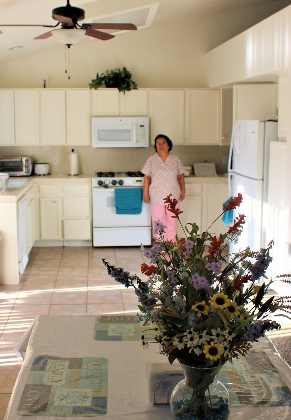 A person stands in a bright kitchen with flowers on the table.