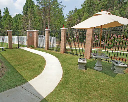 A serene pathway leading through a well-maintained garden with a fence and sunshade.