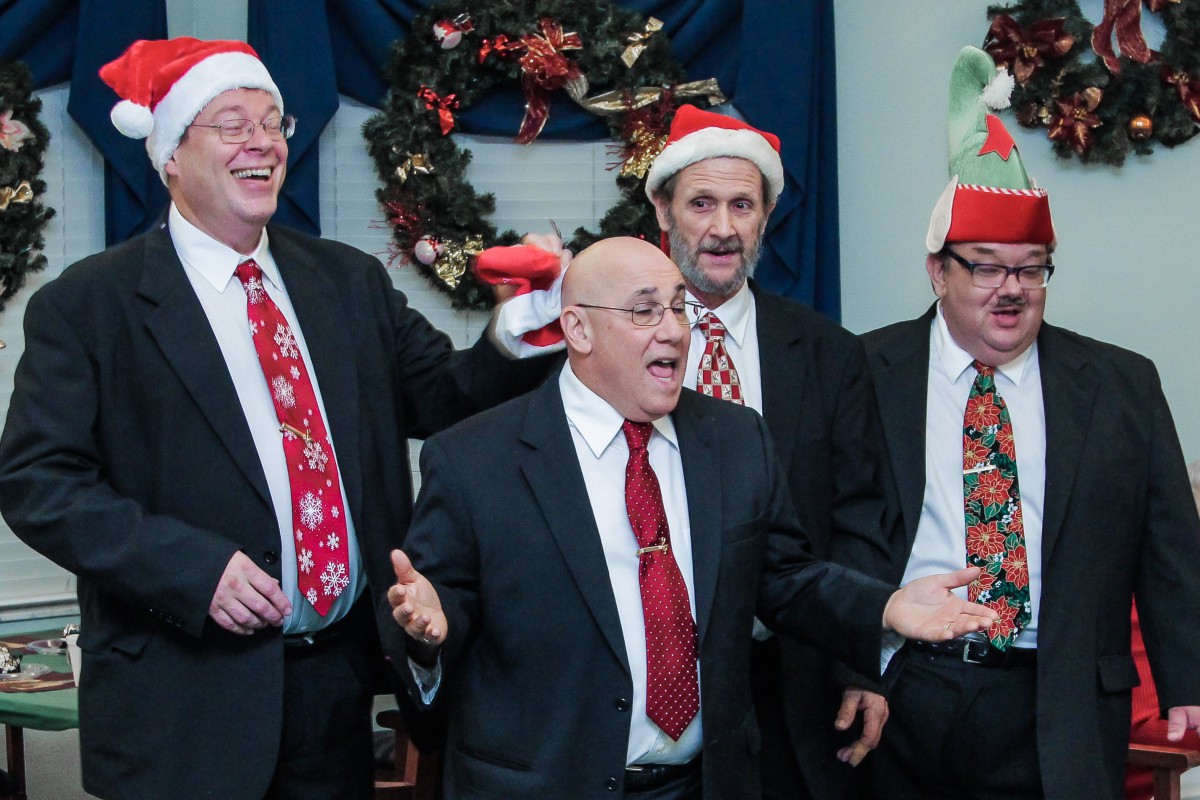A group of men in suits and Santa hats singing during a Christmas celebration.