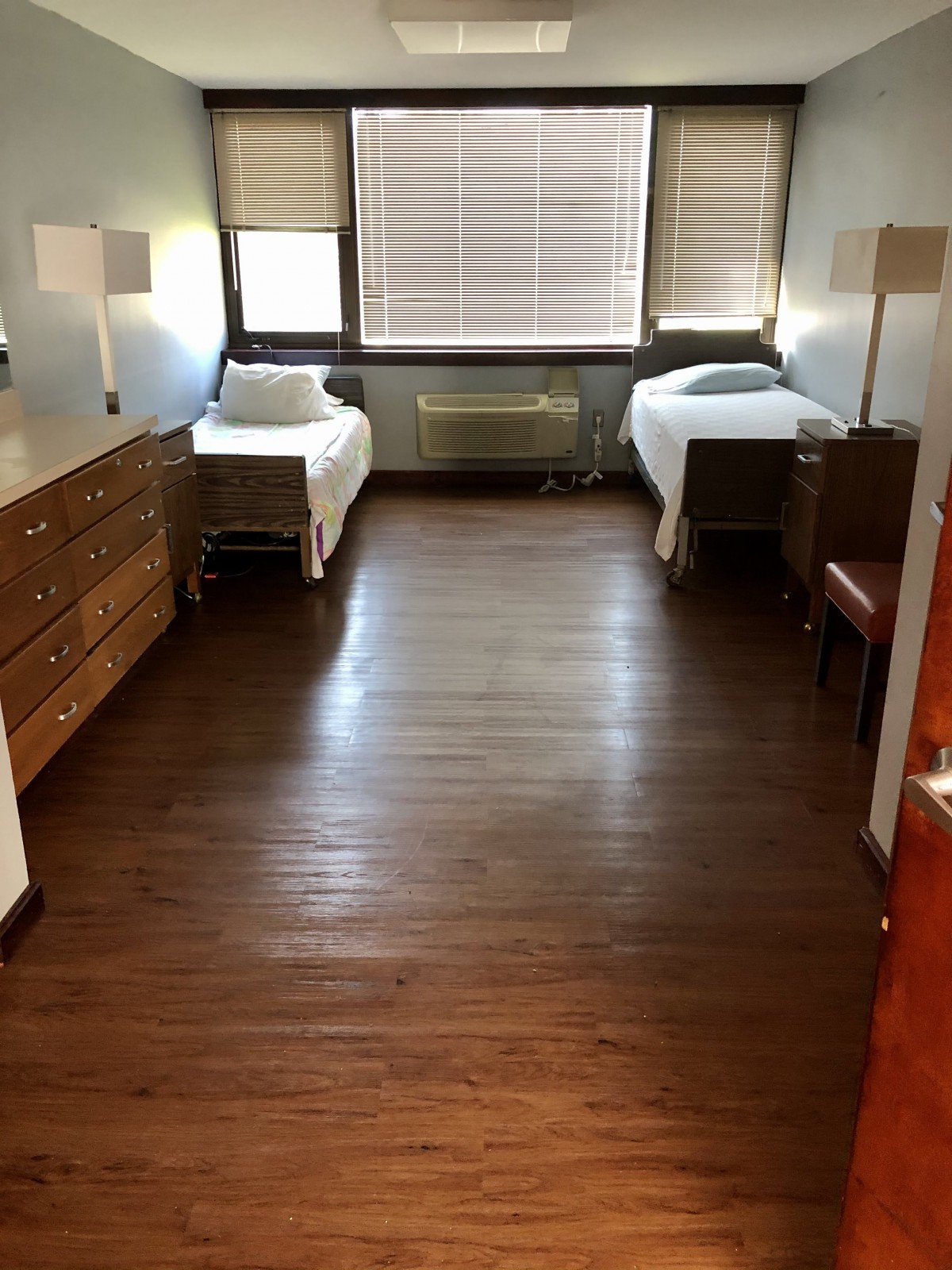 A minimalist dorm room with twin beds, wooden flooring, and simple furnishings.