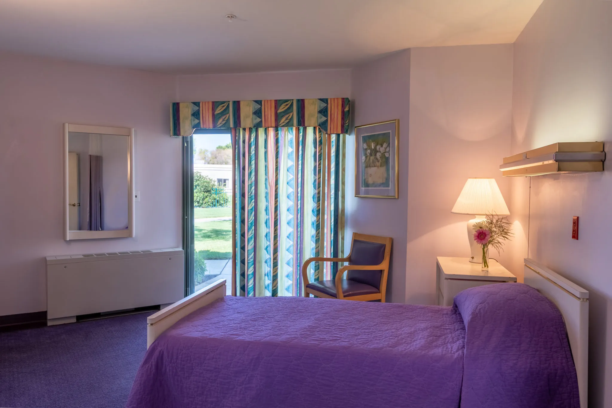 A cozy bedroom with a purple bedspread, a chair, and stylish curtains letting in natural light.