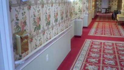 A traditionally styled hallway with floral wallpaper and a red carpet.