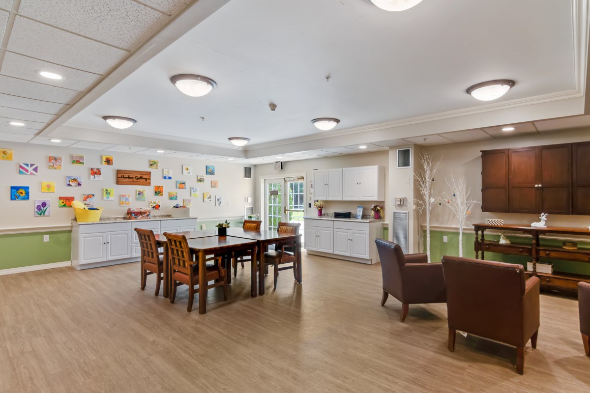 A spacious community dining area with a kitchen, featuring tables and chairs, adorned with colorful wall decorations.