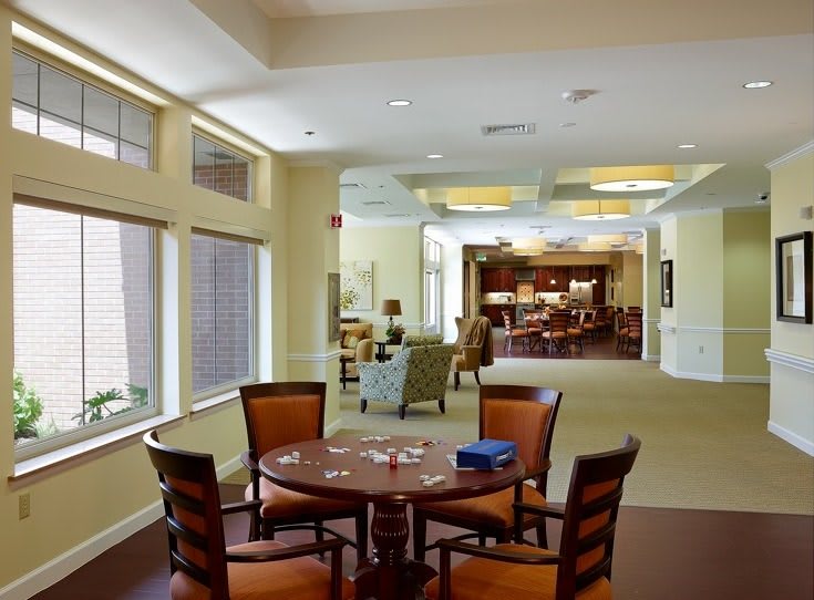 A cozy living room area with a round table and chairs, well-lit by natural light through large windows.