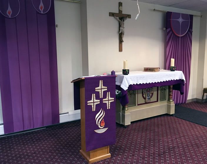 A church interior with an altar and podium adorned with purple drapery and religious symbols.