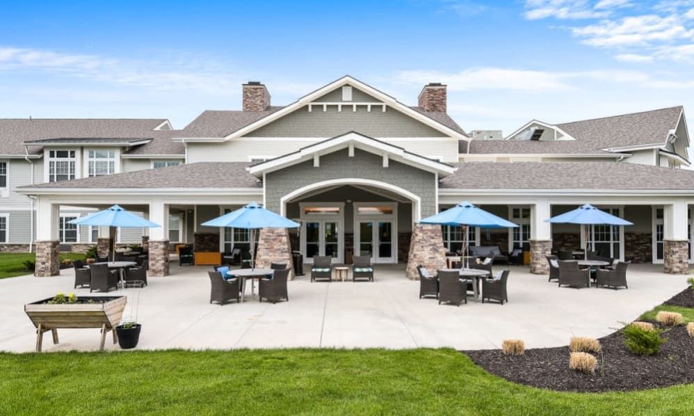 A modern building with outdoor seating on a sunny patio, surrounded by well-maintained landscaping.