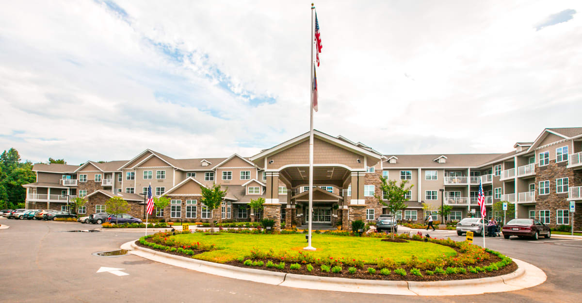 A large building with an American flag at the entrance, surrounded by a landscaped garden and a roundabout under a cloudy sky.
