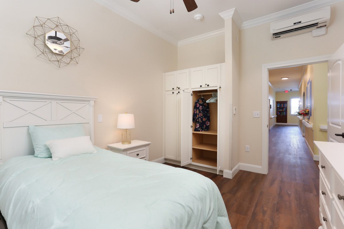A minimalist bedroom with a bed, lamp, and closet on a wood floor.