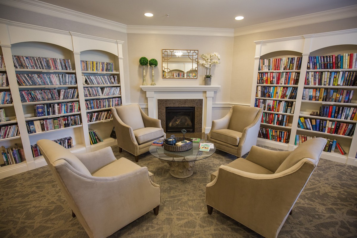 A cozy library room with comfortable seating around a fireplace and shelves filled with books.