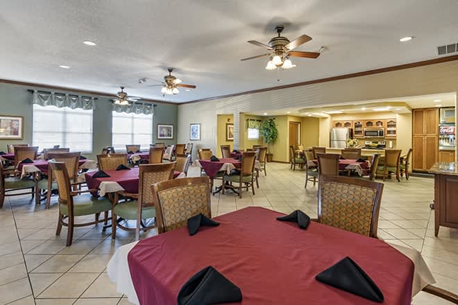 A casual dining room with tables set up for guests, featuring ceiling fans and natural lighting.