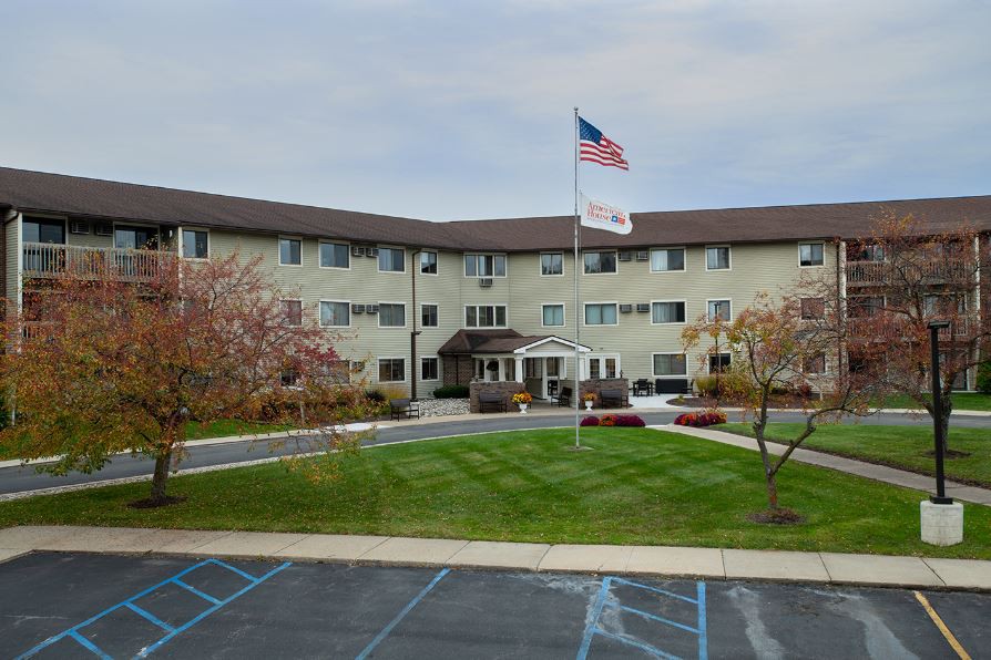 A multi-story building with an American flag in front, surrounded by a landscaped area and parking lot.