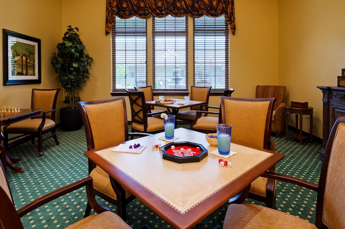 A cozy dining area with tables and chairs, featuring decorative windows and a green carpet.