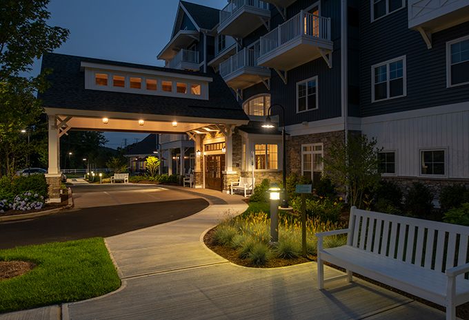 A warmly lit building entrance at night, with a pathway and landscaped surroundings.