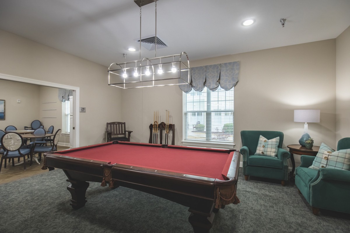 A cozy billiards room featuring a red pool table, elegant lighting, and classic furnishings.