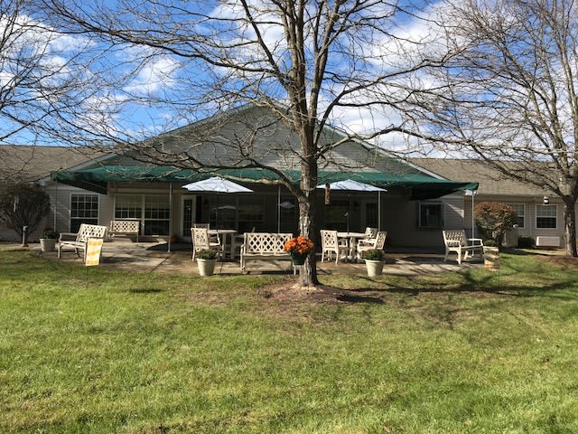 A house with a patio and outdoor furniture, surrounded by a grassy yard and trees on a sunny day.