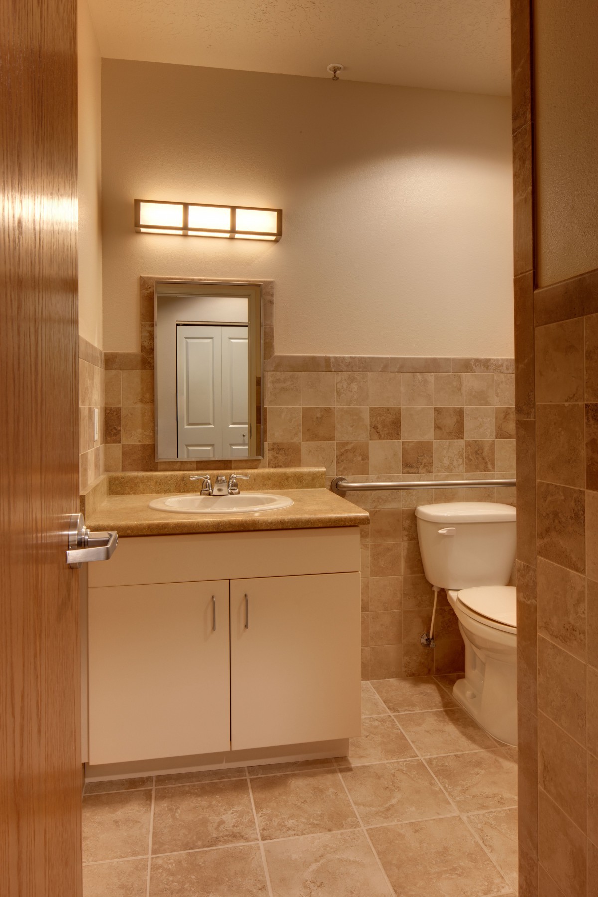 A well-lit bathroom featuring a sink, mirror, and toilet with tiled walls and flooring.
