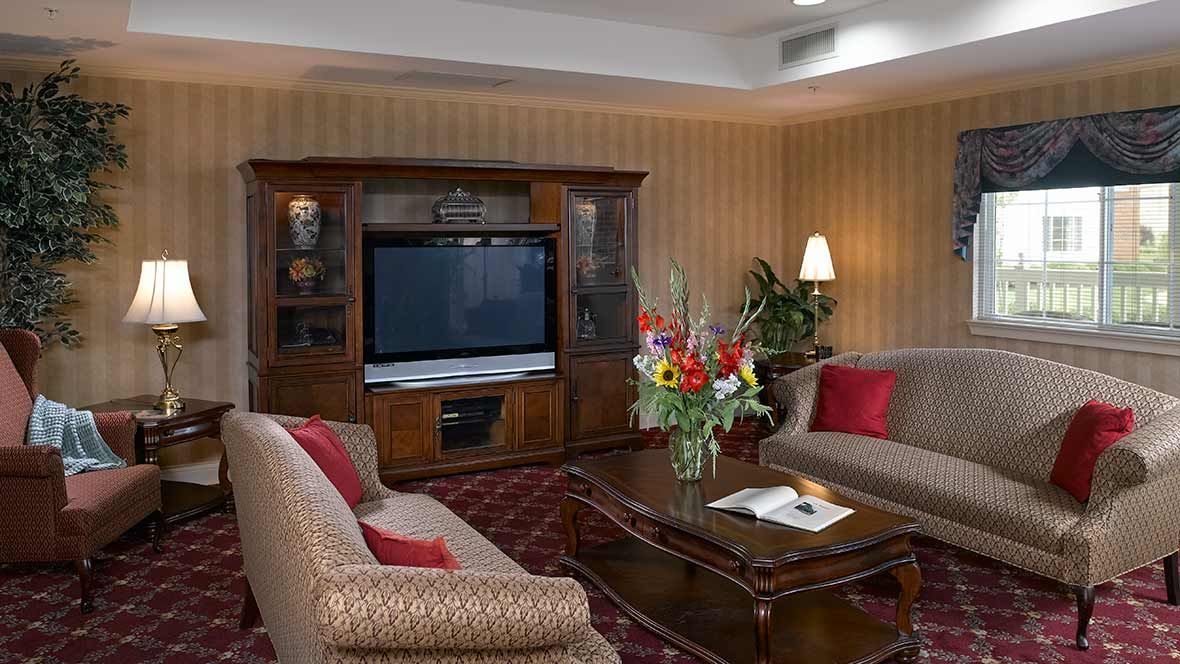 A cozy living room with classic furniture, featuring a large television and a floral centerpiece on the coffee table.