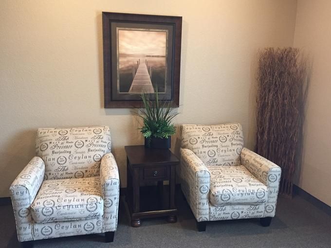 A cozy seating area with two patterned armchairs, a small table holding a plant, and artwork on the wall.