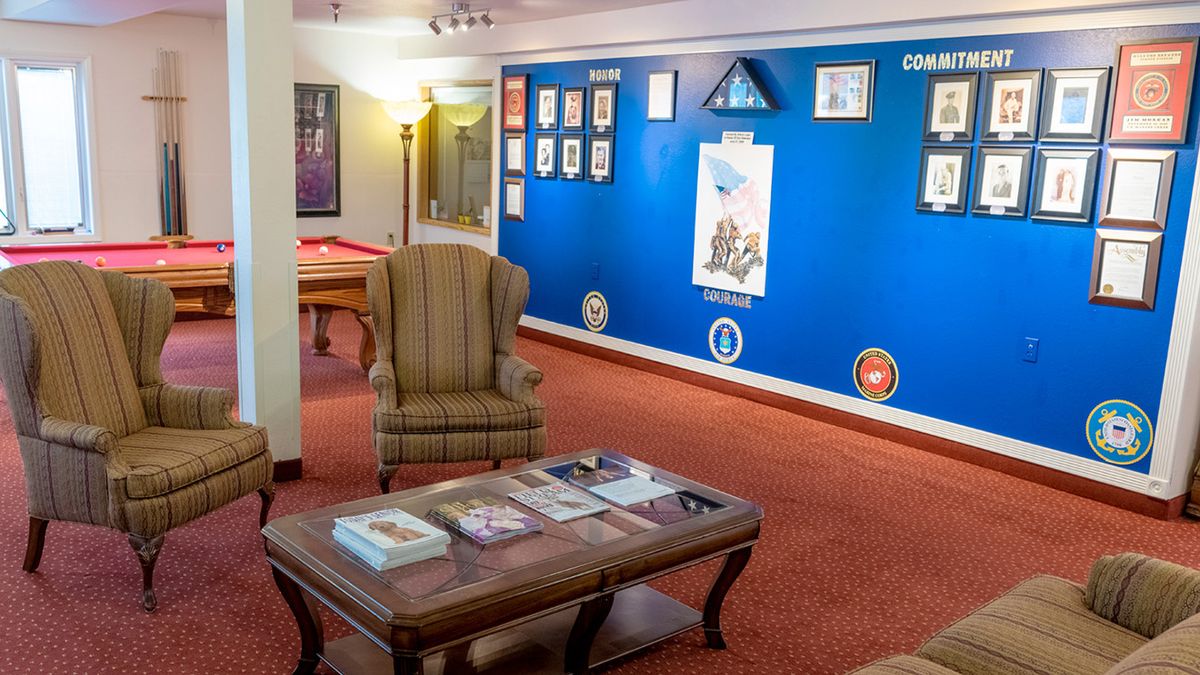 A cozy lounge area with a wingback chair and coffee table, featuring artwork on a blue wall.
