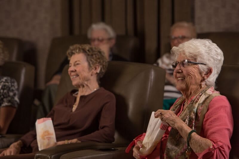 Elderly people enjoying a movie at the theater, sharing laughter and popcorn.