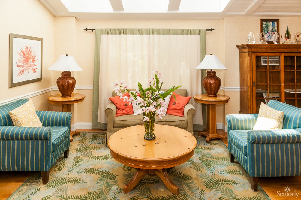 A cozy living room with elegant furniture, featuring a sofa, lamps, and a central coffee table adorned with flowers.