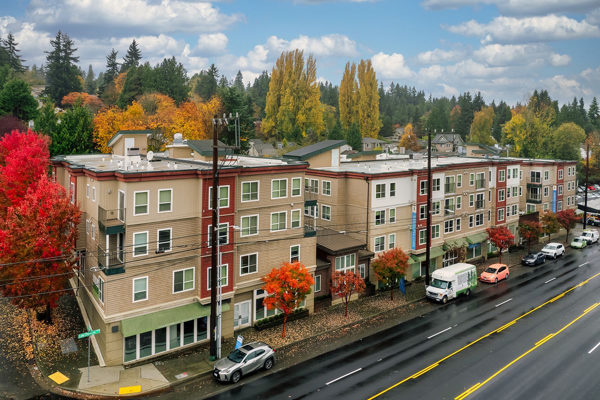 A residential street lined with apartment buildings and colorful autumn trees under a cloudy sky.