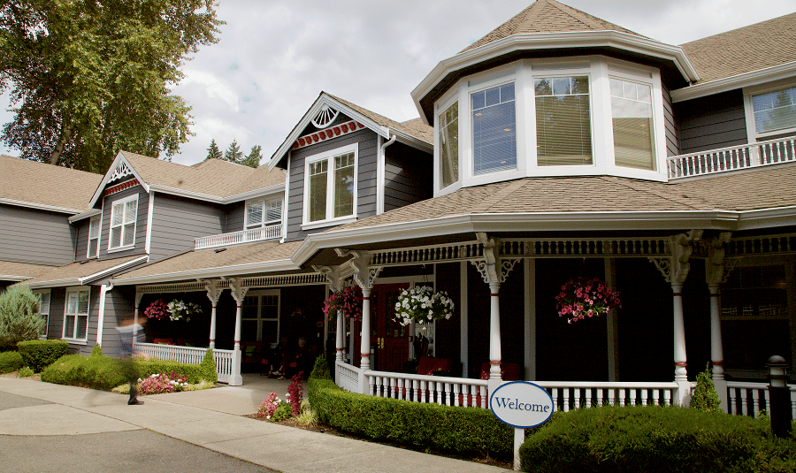 A large, traditional-style house with a welcoming front porch and hanging flower baskets.