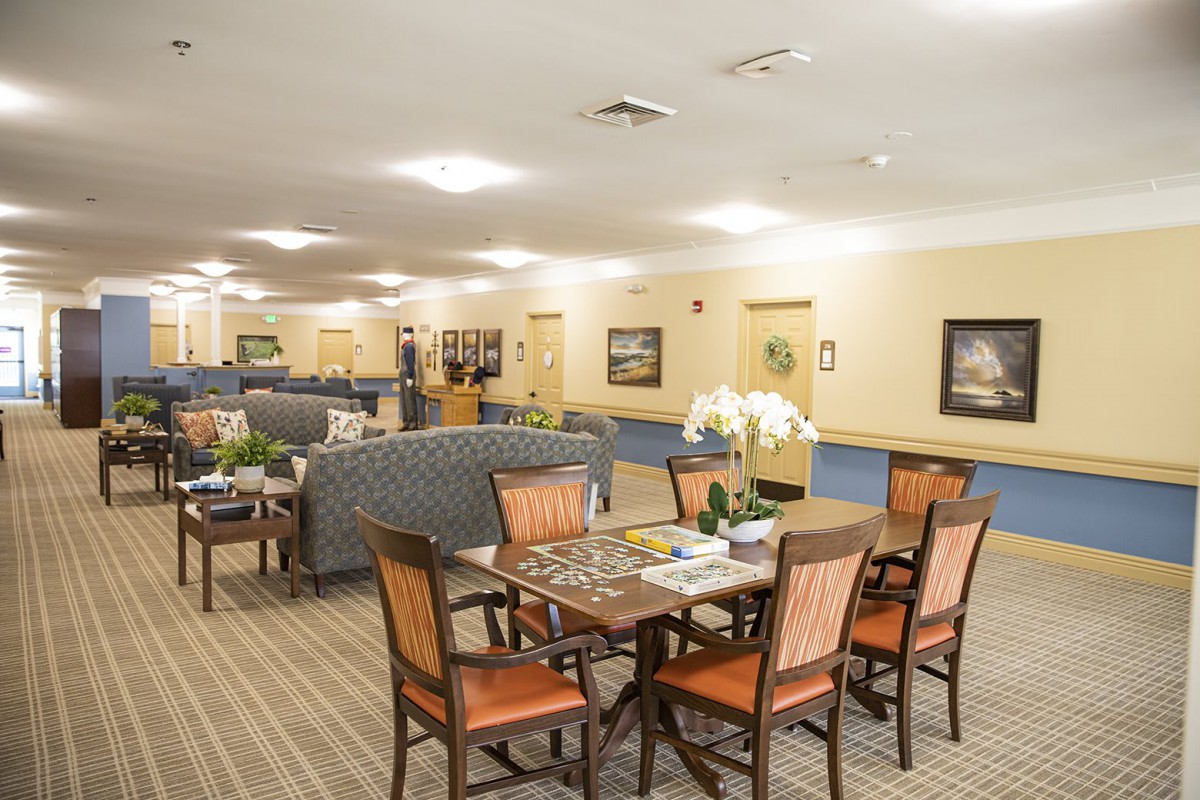 A spacious interior with a dining area featuring a wooden table and chairs, surrounded by comfortable seating and bright lighting.