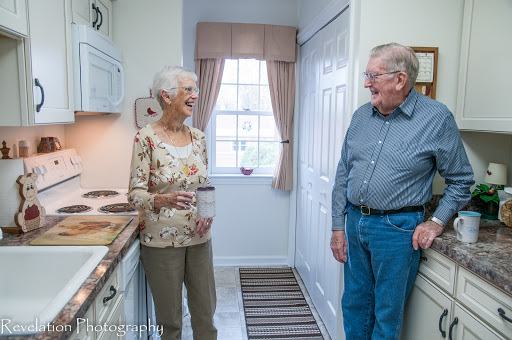 An elderly couple enjoys a lighthearted conversation in their cozy kitchen.