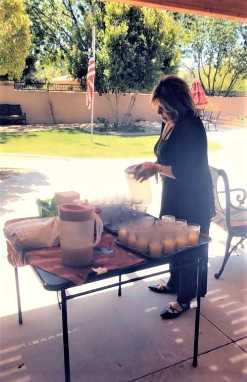 A person setting up a table with beverages and cups outdoors in a garden.