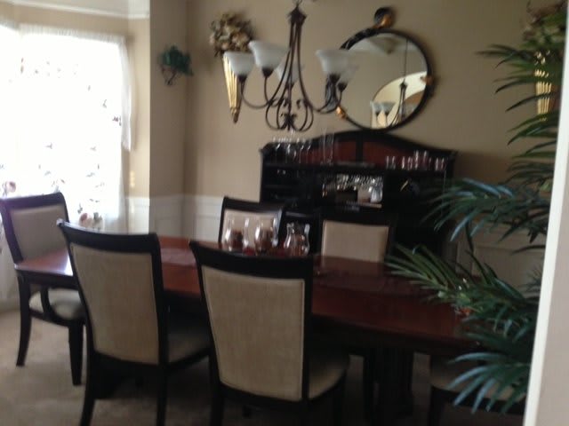 A cozy dining room featuring a wooden table, upholstered chairs, a mirror, and a chandelier.