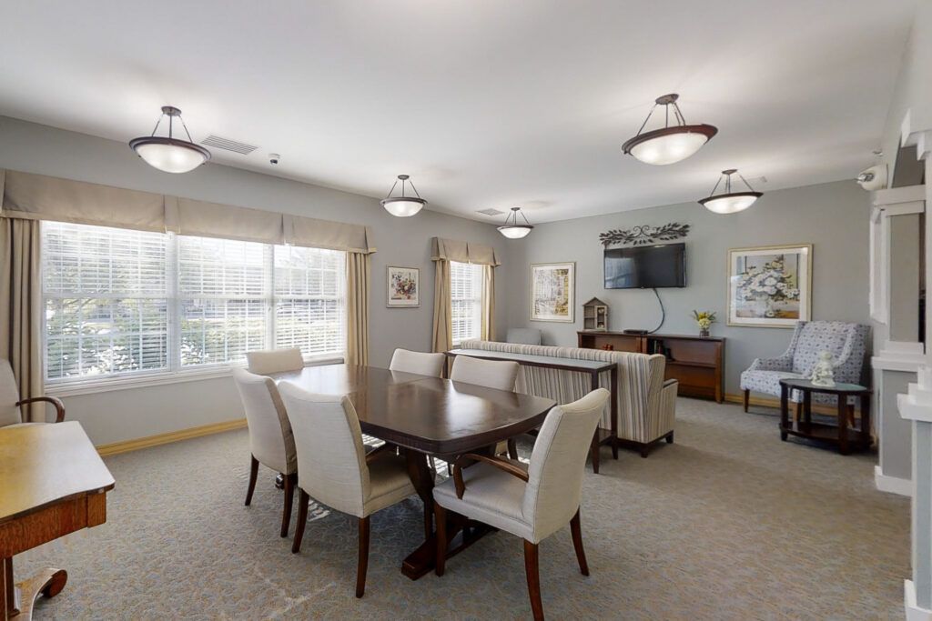 A well-lit dining room with a large table and upholstered chairs, featuring elegant lighting fixtures and decor.