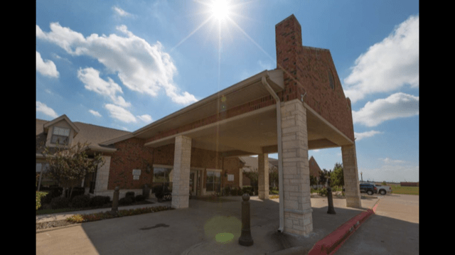 A brick building entrance under a sunny sky with clouds.