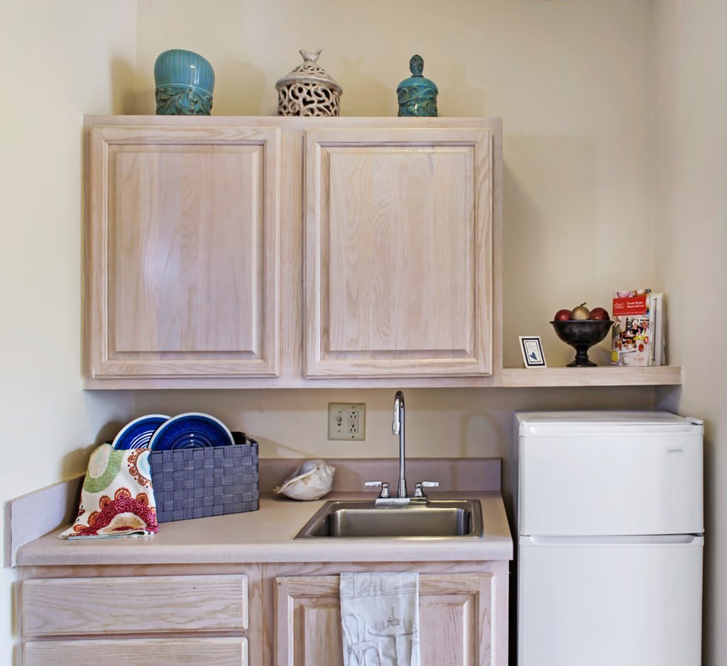 A compact kitchen area with wooden cabinets, a sink, and a small refrigerator.