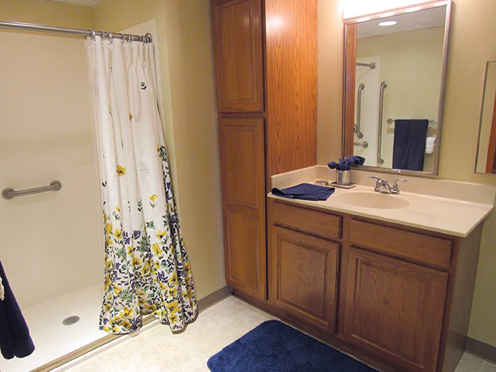 A bathroom with a shower, vanity, and wooden cabinets.