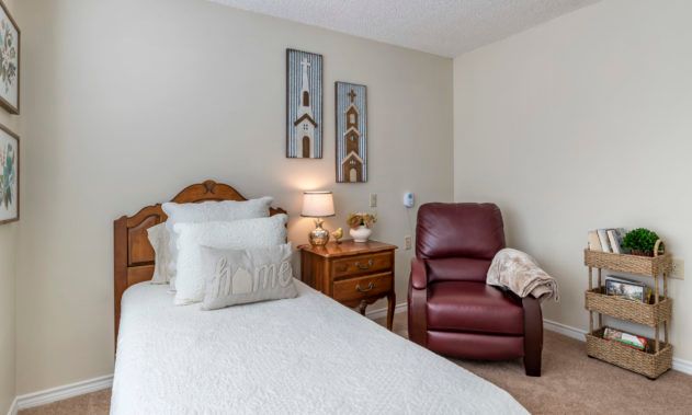 A cozy bedroom with a bed, nightstand, lamp, and a recliner chair.