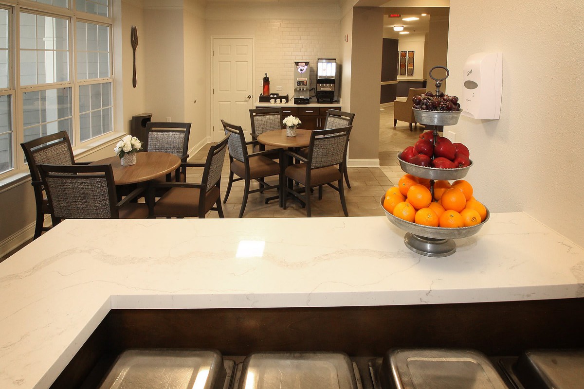 A cozy dining area with tables, chairs, and a fruit bowl on the counter.