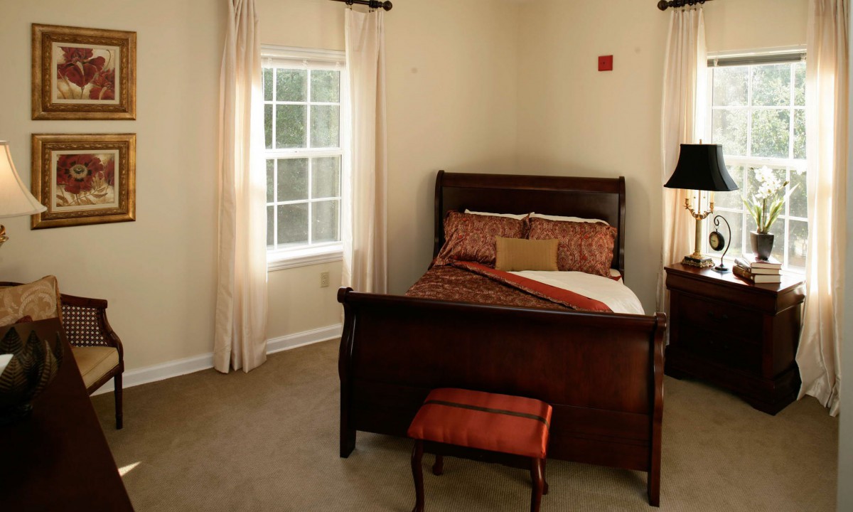 A cozy bedroom with a wooden bed frame, bedside table, and a window with curtains.