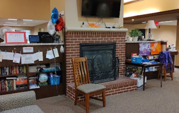 A cozy living room setting with a brick fireplace, wooden chair, and a television mounted above.