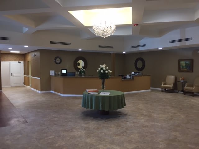 A spacious lobby featuring a central table with floral arrangements and a chandelier.