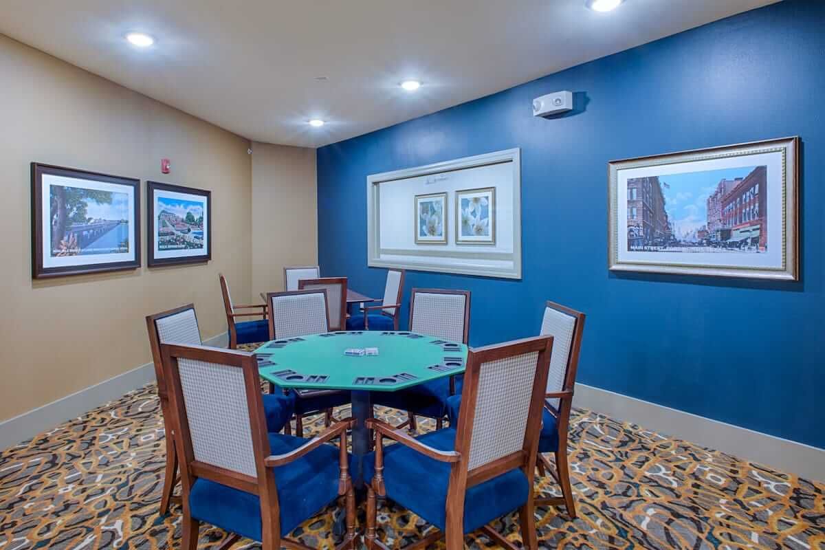 A well-lit game room featuring a poker table surrounded by chairs and decorated with framed wall art.