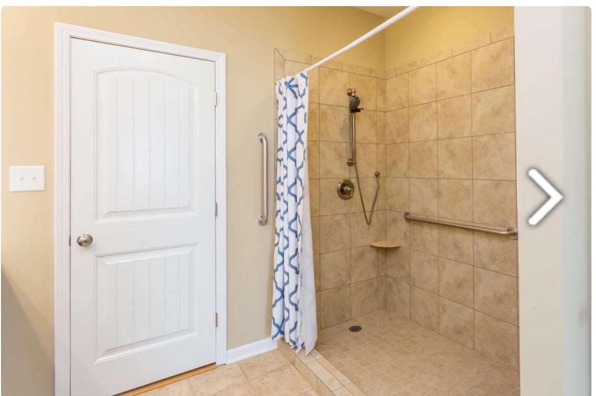 A bathroom with a walk-in shower featuring tiled walls, a patterned curtain, and a safety grab bar.