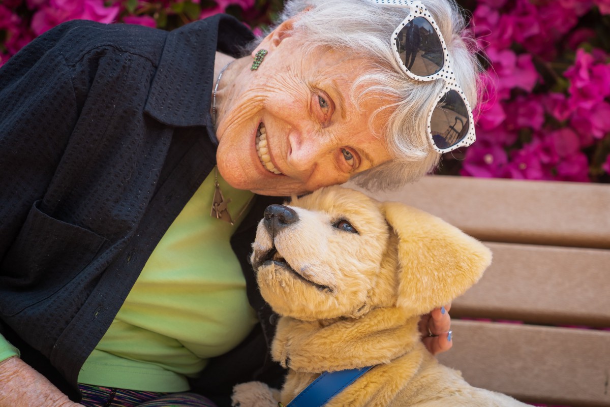 An elderly woman smiles while sitting outdoors with her dog.