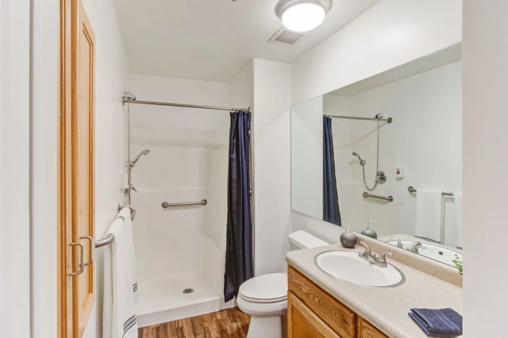 A clean and modern bathroom with a shower, sink, toilet, and large mirror.