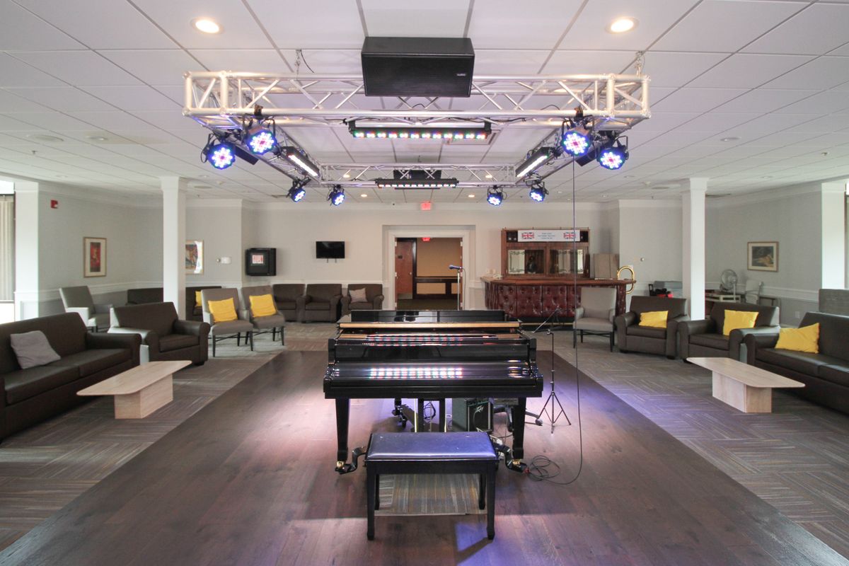 A modern lounge area featuring a piano and stage lighting, surrounded by comfortable seating.