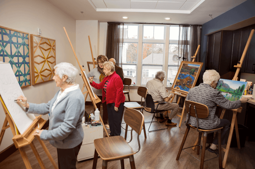 A group of seniors participating in an art class, painting on canvases set up on easels.