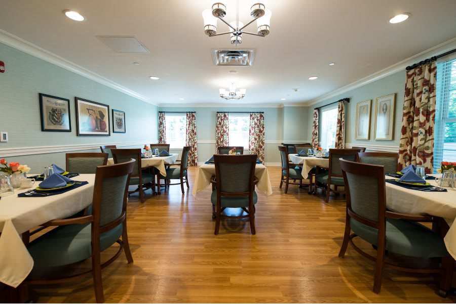A well-lit dining room with wooden floors, arranged with multiple tables and chairs.